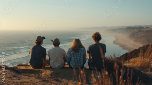 A group of friends sit atop a lookout point backs turned to the camera as they gaze out at the vast unending ocean stretching . .