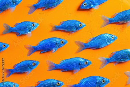 School of Small Blue Fish Swimming Together in Harmony on Vibrant Orange Background
