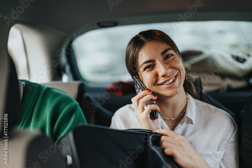 A happy young woman is seen talking on her smart phone in the backseat of a vehicle, conveying a sense of connectivity and mobility.