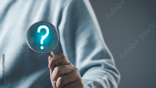 The concept of finding an answer to complex questions in business. Hand holding a magnifying glass with question mark. 