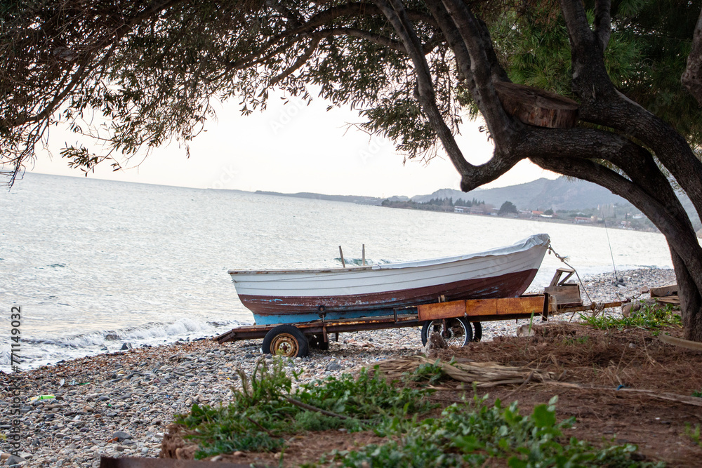 Old fishing boat on the pebble beach in the evening. Old fishing boat on a cart on the beach at sunset.