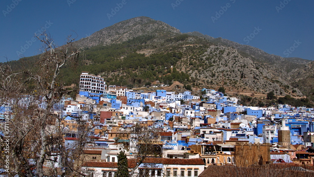 Blue and white houses in a hill in the medina, in Chefchaouen, Morocco, with mountains rising up in the background