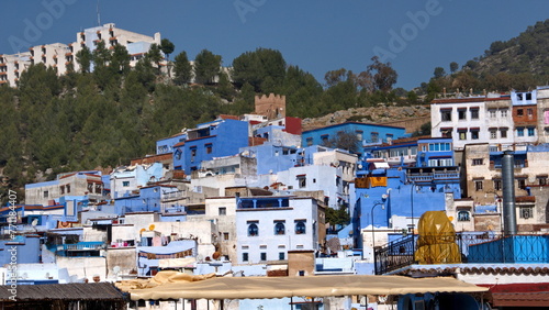 Blue and white houses in a hill in the medina, in Chefchaouen, Morocco, with mountains rising up in the background © Angela