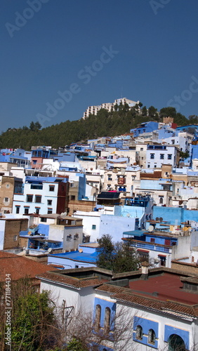 Blue and white houses in a hill in the medina, in Chefchaouen, Morocco, with mountains rising up in the background