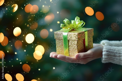 Hands holding little gold gift with green bow on festive lights bokeh © kuzenkova