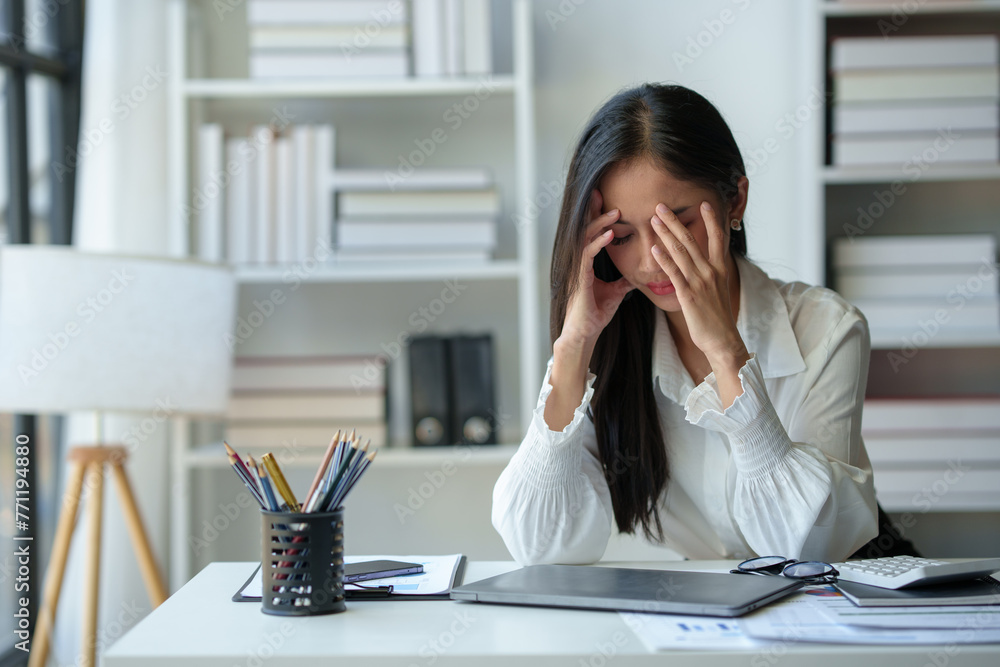 Asian businesswoman is tired, headache, sleepy and bored from sitting at a desk for a long time working on a laptop computer. Problematic financial paperwork Office syndrome concept. Asian businesswoman is tired, headache, sleepy and bored from sitting at a desk for a long time working on a laptop computer. Problematic financial paperwork Office syndrome concept.