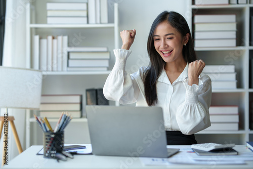 Asian businesswoman, office worker happy and cheerful while receiving recognition on laptop computer, expressing excitement over success and company annual bonus. Success concept.