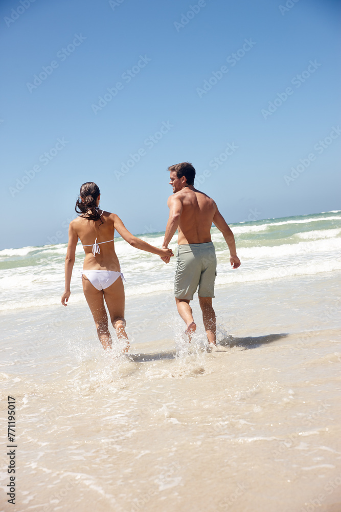 Couple, rear view and holding hands in water with travel for bonding, summer vacation and anniversary getaway. Man, woman and love by ocean with swimwear for walking, healthy relationship or blue sky Couple, rear view and holding hands in water with travel for bonding, summer vacation and anniversary getaway. Man, woman and love by ocean with swimwear for walking, healthy relationship or blue sky