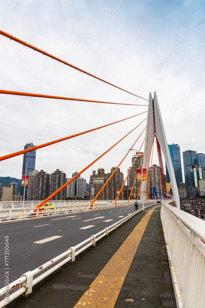 The Qiansimen Bridge, the Yangtze River Bridge in Chongqing, China, features vehicles driving on the bridge and towering skyscrapers in the distance