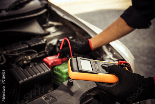 Hand car mechanic holding voltmeter to check voltage car battery energy problem for service maintenance and re charger or jump start or change battery replacement.