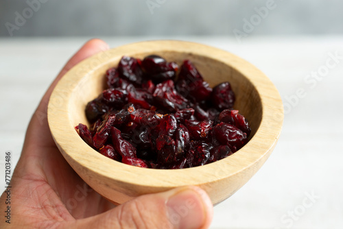 A view of a hand holding wood condiment cup of dried cranberries.