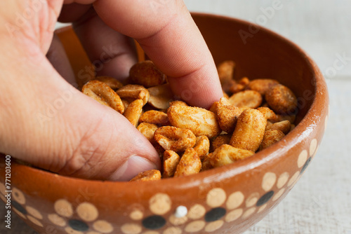 A closeup view of a hand grabbing roasted peanuts from a clay bowl.