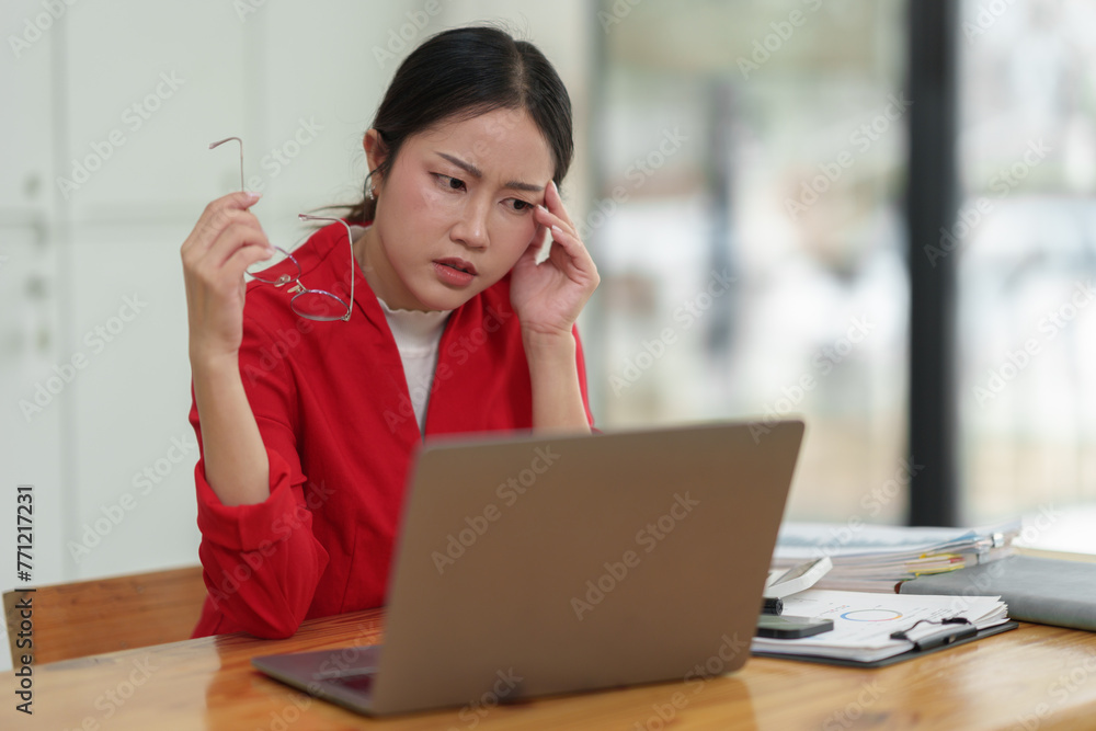 Young independent businesswoman with glasses is tired, stressed, has a headache while sitting in front of a laptop for a long time and working in finance. Online. Office Syndrome concept. Young independent businesswoman with glasses is tired, stressed, has a headache while sitting in front of a laptop for a long time and working in finance. Online. Office Syndrome concept.