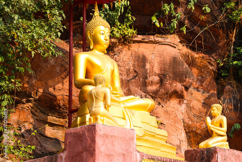 Golden Buddha statue in the background is a rock cliff.