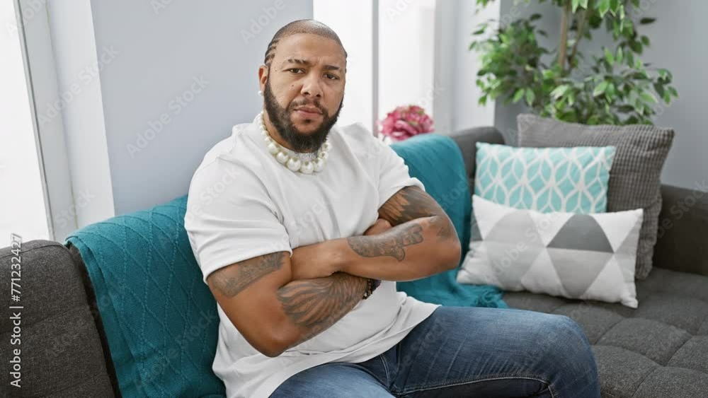 Nervous african american man expressing doubt with a skeptic frown, sitting in the living room with crossed arms, disapproving look. portrait of a negative emotion at home Nervous african american man expressing doubt with a skeptic frown, sitting in the living room with crossed arms, disapproving look. portrait of a negative emotion at home
