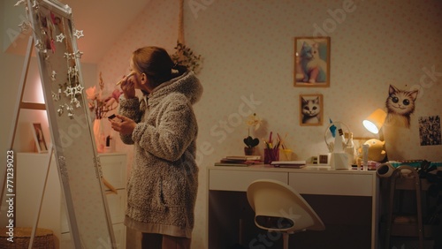 Wallpaper Mural Young Caucasian girl does eyebrows makeup standing and looking in the mirror in cozy and comfort bedroom. Teenage girl spending leisure time and having fun at home at night. Concept of lifestyle. Torontodigital.ca