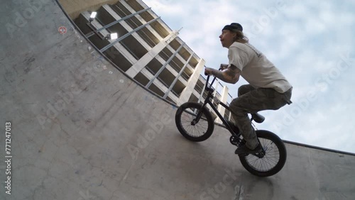 BMX biker riding sideways along the top of skatepark bowl in 800fps extreme slow-motion, sunrise fisheye lens tracking shot photo