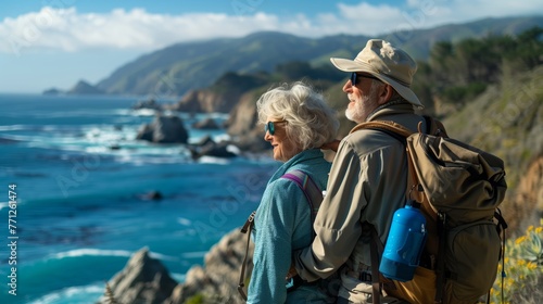 Elderly senior smiling active couple with backpacks enjoying hiking and walking along coastline near mountains and sea or ocean, active retirement lifestyle filled with outdoor adventures.
