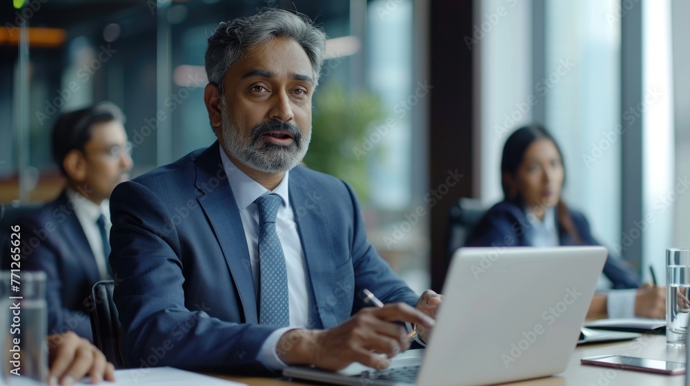 Successful Indian CEO Making a Presentation on a Laptop to a Board of Directors During a Corporate Meeting. South Asian Business Partners Discussing International Markets Successful Indian CEO Making a Presentation on a Laptop to a Board of Directors During a Corporate Meeting. South Asian Business Partners Discussing International Markets