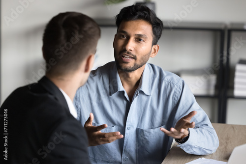 Inspired young Indian entrepreneur man talking to business partner, consulting financial specialist, legal expert at office workplace. Project manager explaining job task to colleague