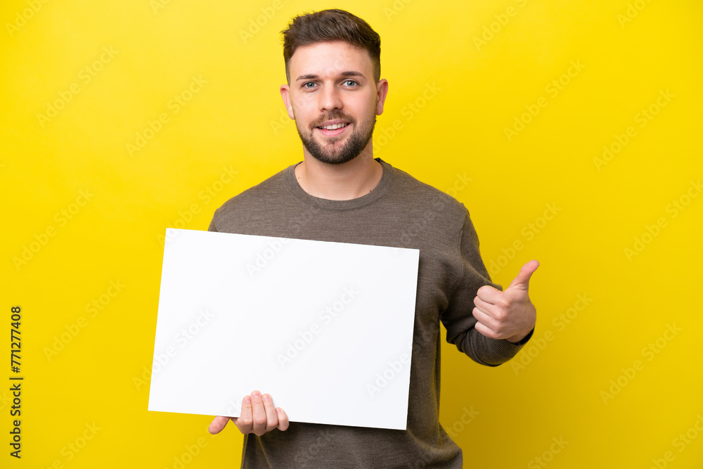 Young caucasian man isolated on yellow background holding an empty placard with thumb up Young caucasian man isolated on yellow background holding an empty placard with thumb up