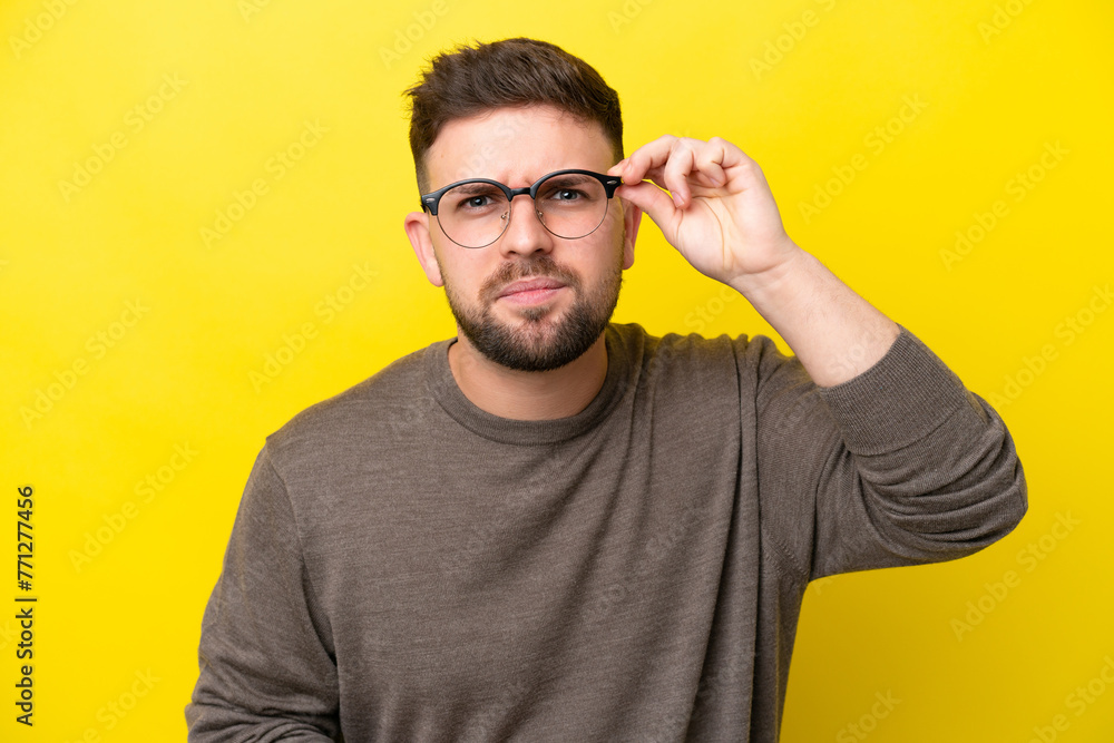 Naklejka premium Young caucasian man isolated on yellow background With glasses and frustrated expression