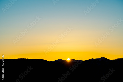 山の稜線から昇る眩しい太陽と美しい朝焼けの空。