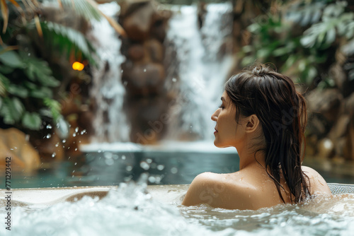 A woman is in a hot tub with a waterfall in the background