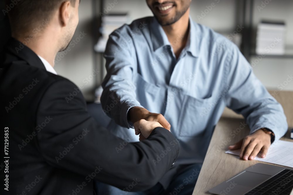 Happy diverse young business partners men giving handshake at workplace, smiling, thanking for consultation, professional advice, trust. Businessmen shaking hands close up Happy diverse young business partners men giving handshake at workplace, smiling, thanking for consultation, professional advice, trust. Businessmen shaking hands close up