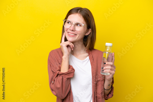 Young English woman with a bottle of water isolated on yellow background thinking an idea while looking up