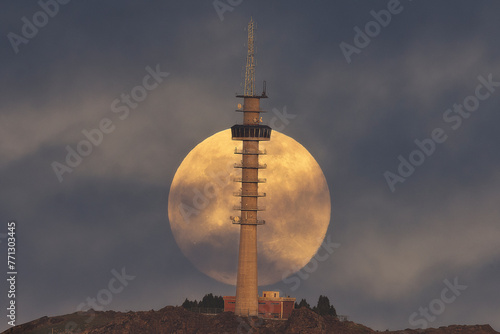 A large full moon rising behind an antenna tower on Mount Mendibil, Bizkaia, moments before sunset photo