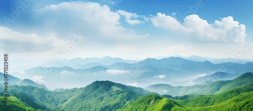 A scenic landscape with green mountains stretching into the distance under a beautiful sky filled with fluffy white clouds, viewed from a high vantage point