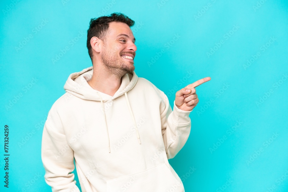 Young caucasian handsome man isolated on blue background pointing finger to the side and presenting a product Young caucasian handsome man isolated on blue background pointing finger to the side and presenting a product