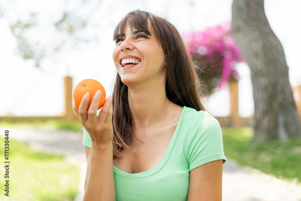 Young woman at outdoors holding an orange with happy expression Young woman at outdoors holding an orange with happy expression