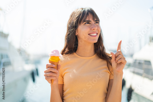 Young woman with a cornet ice cream at outdoors intending to realizes the solution while lifting a finger up