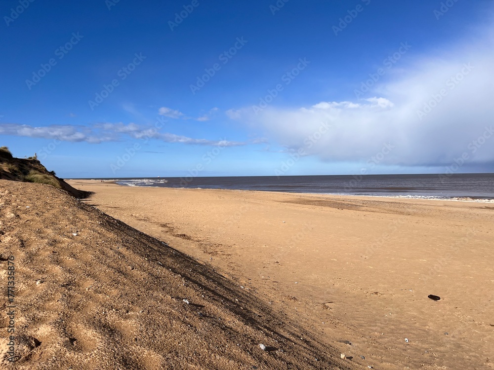 Obraz premium Beautiful landscape view of the vast sandy beach in Norfolk East Anglia uk with clear blue skies white cloud storm approaching calm rolling waves of sea and no people