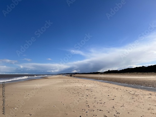 Beautiful landscape view of the vast sandy beach in Norfolk East Anglia uk with clear blue skies white cloud storm approaching calm rolling waves of sea and no people