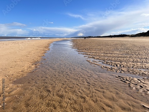 Stunning beautiful coast landscape of white sandy beach at low tide inlet river on shore to horizon with couple walking blue sky calm sea and white cloud Spring cold fresh day at Winterton Norfolk uk 