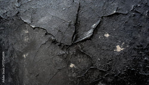 A close-up black and white shot of a cracked wall showing signs of deterioration and wear. The cracks cut through the concrete surface, creating a striking contrast between the dark shadows and light photo
