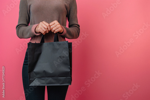 woman holding a black shopping bag against pink backgro efa8916a-20b0-443b-a6e4-0881f6b2d93e photo