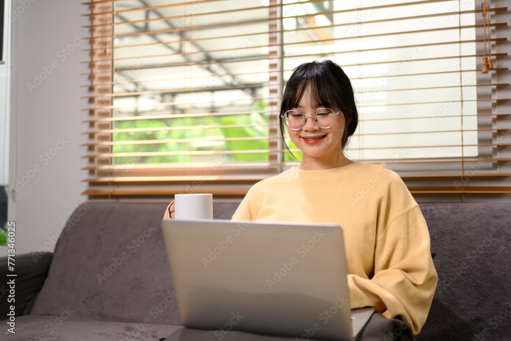 Pretty young chubby woman holding cup of tea and using laptop on sofa at home Pretty young chubby woman holding cup of tea and using laptop on sofa at home