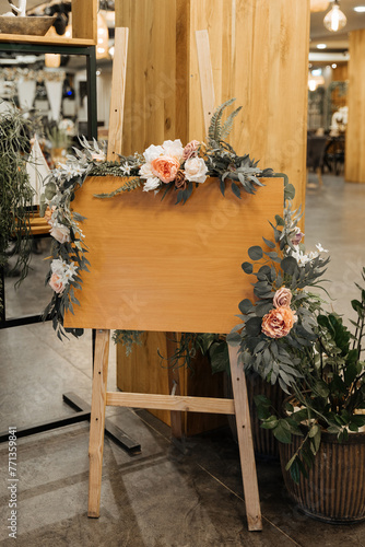 A wooden welcome sign covered in colorful flowers and lush greenery, creating a vibrant and inviting display. 