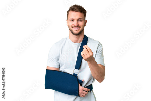 Young caucasian man with broken arm and wearing a sling over isolated chroma key background making money gesture
