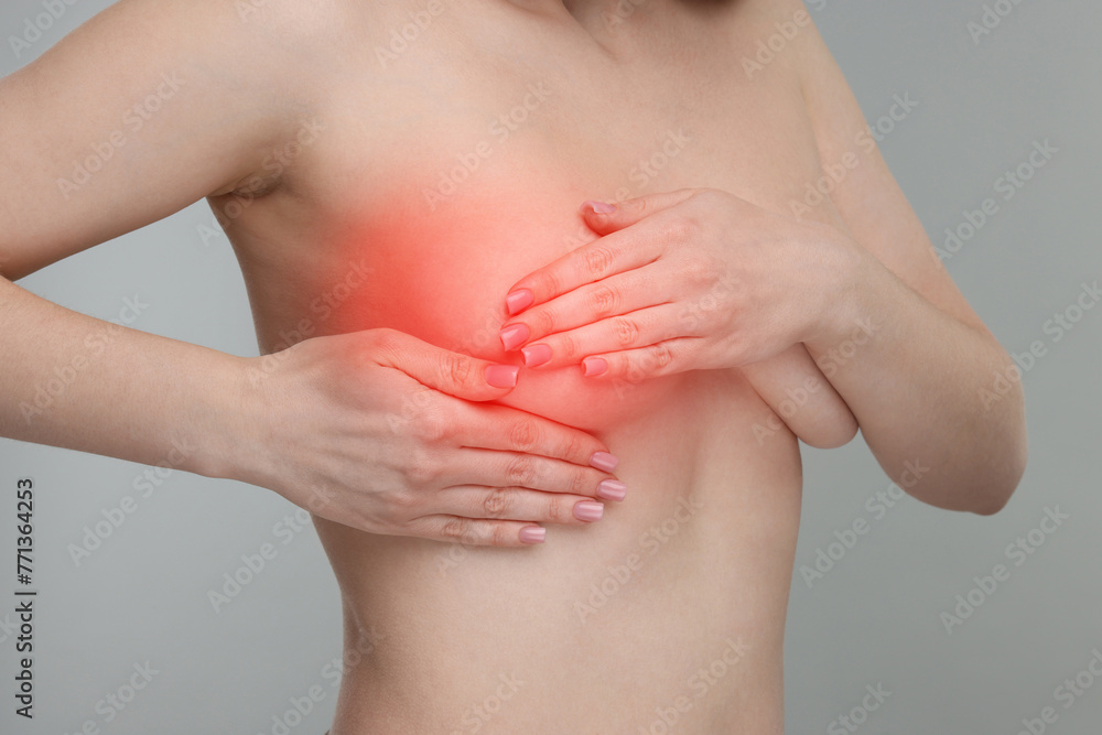 Naked young woman suffering from breast pain on light grey background, closeup