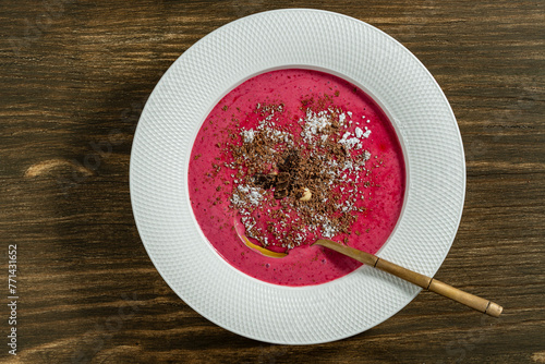 Sweet summer cherry soup in a white plate on a wooden background, closeup, top view. Hungarian cold red cherry soup with yogurt or cream, sprinkled with grated chocolate, powdered sugar and hazelnuts
