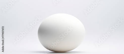 A spherical white egg is resting on a smooth white surface, resembling a ball or sports equipment. The contrast between the egg and the ceiling creates a visually striking event © AkuAku