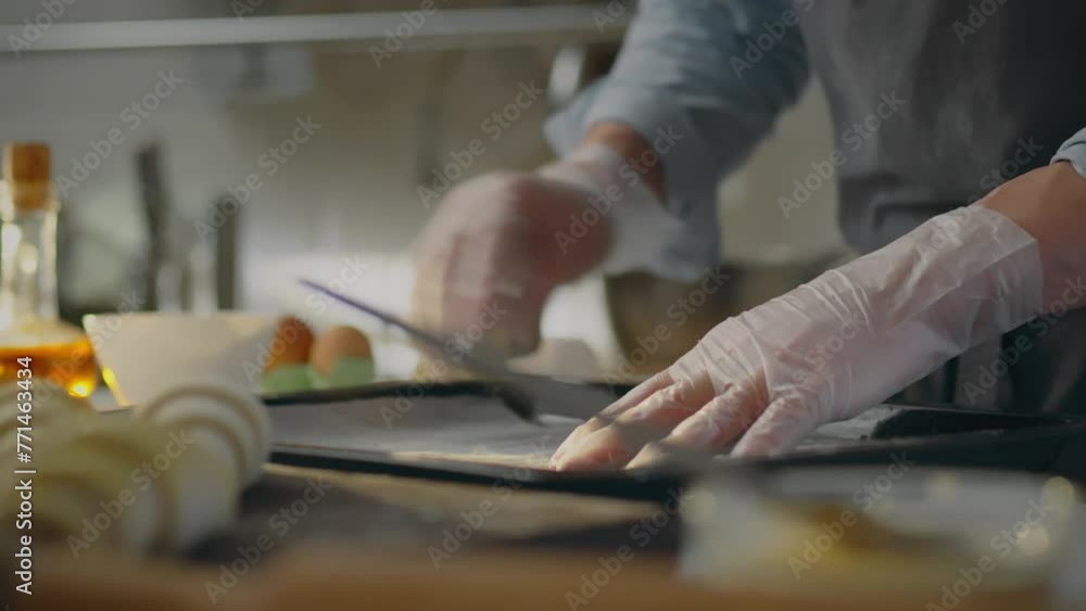 Bakery. The chef, dressed in comfortable work clothes, concentrates on placing parchment on baking sheet in the bakery. A modern man prepares baking tray in the oven, masters new baking recipes, fresh Bakery. The chef, dressed in comfortable work clothes, concentrates on placing parchment on baking sheet in the bakery. A modern man prepares baking tray in the oven, masters new baking recipes, fresh