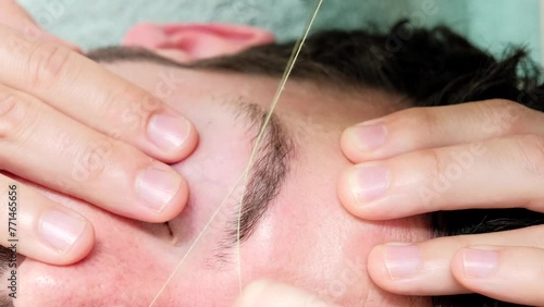 Horizontal 4K close up video of a male eyebrow waxing with threading on a young woman in a beauty salon. Concept of wellness and body care