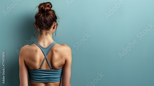 Woman in a sports bra viewed from the back, standing against a blue wall.