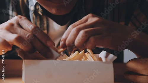 Closeup image of a woman holding and eating french fries and hamburger with fried chicken on the table at home photo
